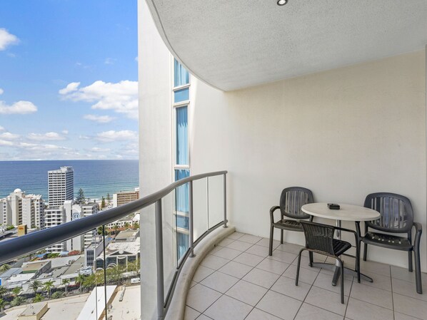 A balcony with a view of the ocean and cityscape, featuring a table and two chairs.