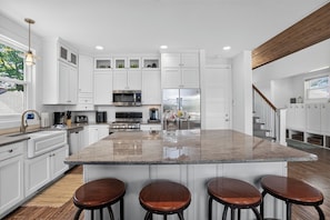 A modern kitchen with white cabinetry, stainless steel appliances, a large island with stools, and a wooden ceiling.