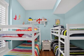 Un dormitorio infantil con literas, una mesita de noche pequeña y una estantería con juguetes y adornos.