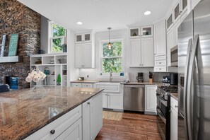 Una cocina moderna con armarios blancos, encimeras de granito, un refrigerador de acero inoxidable y un lavavajillas integrado.