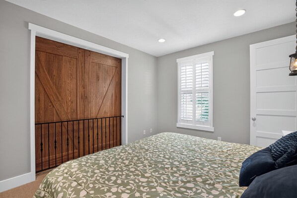 Un dormitorio con una cama grande, un armario de madera, una ventana con persianas y una puerta.