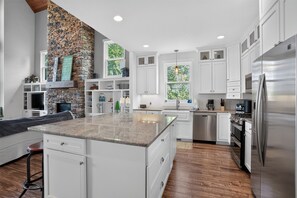 Una cocina moderna con armarios blancos, una pared de acento de piedra y una isla grande con encimera de granito.