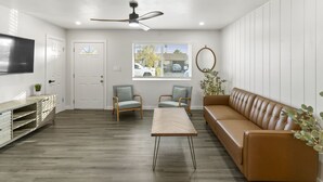Una sala de estar moderna con un sofá, dos sillones, una mesa de centro, un televisor y un ventilador de techo.