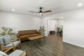 A modern living room with a brown leather sofa, two grey armchairs, a wooden coffee table, and a ceiling fan.