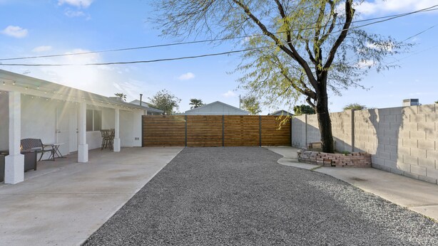 Un patio techado con un sendero de grava, una cerca de madera y un muro de ladrillo.