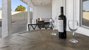 Un espacio de comedor al aire libre techado, con una mesa, una botella de vino y copas.
