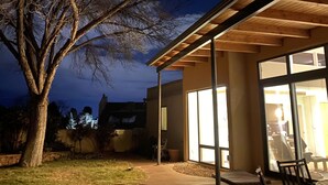 A modern building with a covered patio area, large windows, and a tree in the foreground.