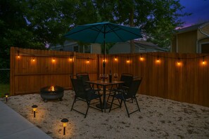 Eine Terrasse im Freien mit Tisch und Stühlen, umgeben von einem Holzzaun und Lichterketten.