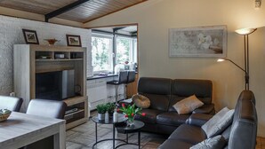 A cozy living room with a fireplace, a sofa, a dining table, and a kitchen area visible through an open door. - Ferienhaus schöne Aussicht (Gerolstein)