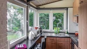 A compact kitchen with a window, a kettle, a sink, and wooden cabinets. - Ferienhaus schöne Aussicht (Gerolstein)