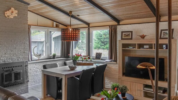 A cozy living room with a fireplace, a dining area with a table and chairs, and a large window with curtains. - Ferienhaus schöne Aussicht (Gerolstein)
