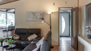 A living room with a leather sofa, a side table with a vase of flowers, a floor lamp, and a framed picture on the wall. - Ferienhaus schöne Aussicht (Gerolstein)