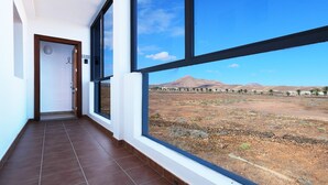 Un pasillo con grandes ventanales, una puerta y vistas a un paisaje árido con montañas.