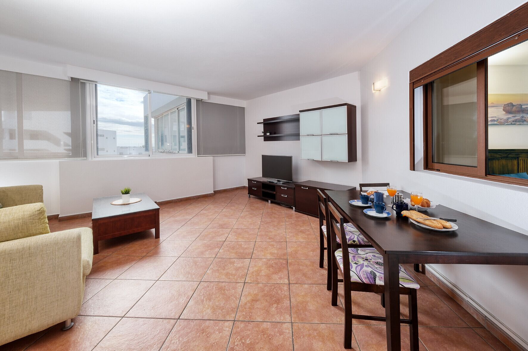 Un espacio habitable compacto con kitchenette, zona de comedor y área de estar con sofá y una mesita.