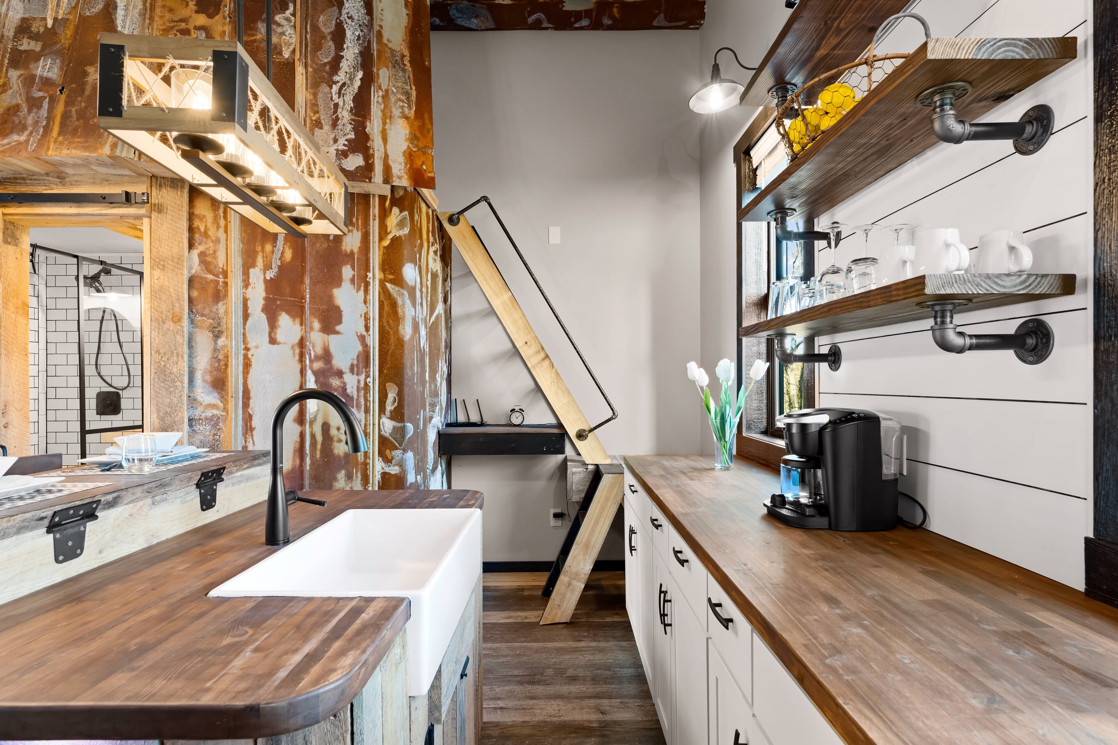 A kitchen with a wooden countertop, a sink, and a coffee maker. There is a wooden ladder leaning against the wall and a shelf with glassware.