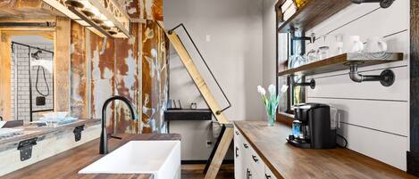 A kitchen with a wooden countertop, a sink, and a coffee maker. There is a wooden ladder leaning against the wall and a shelf with glassware.