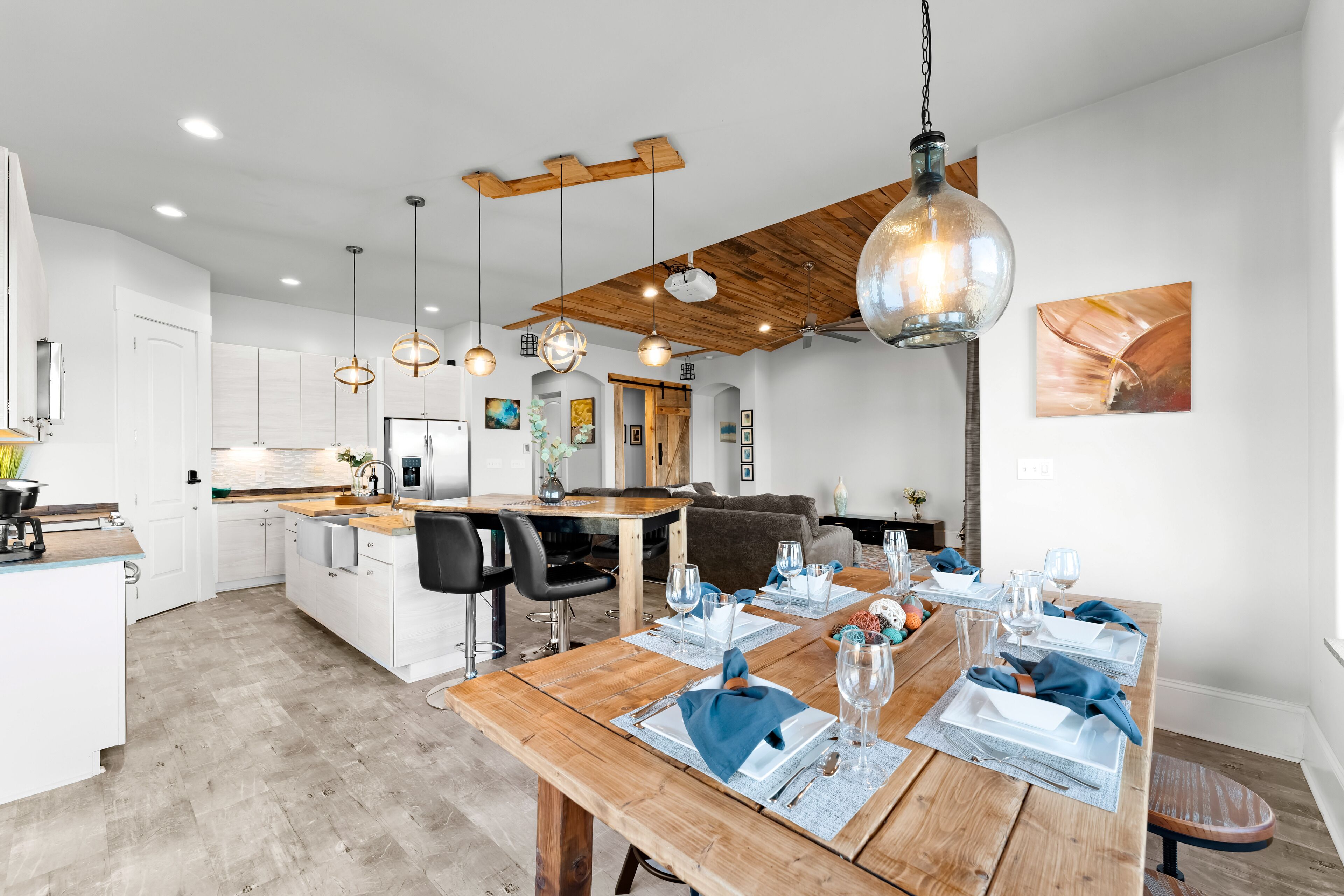 A modern kitchen with white cabinets, a wooden dining table set for four, and pendant lights.