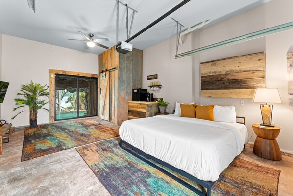 A modern bedroom with a large bed, a ceiling fan, a coffee bar, and a view of the outdoors. - Nancy Key w/Pool, Wine Cave, Optional Boat Rental (Sherrills Ford)