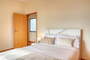 Ein Schlafzimmer mit Bett, Holztür, Nachttisch und Fenster.