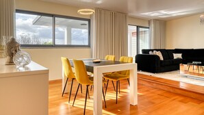 Ein modernes Wohnzimmer mit Essbereich, großen Fenstern und einem schwarzen Sofa.