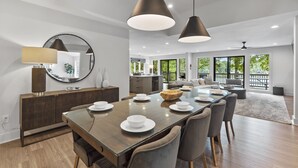 Uma sala de jantar moderna com uma mesa grande, cadeiras e luminárias pendentes.