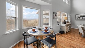 A dining area with a round table, four chairs, and a view of the outdoors through large windows. - Mountain Cottage on Ski Slopes (Blowing Rock)