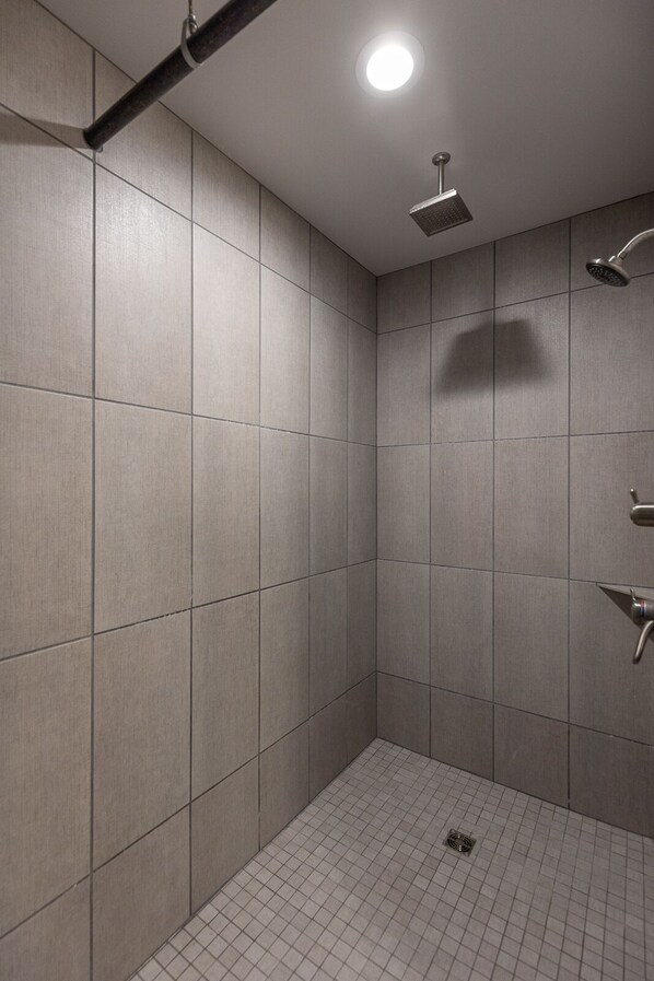 Een moderne badkamer met betegelde wanden en vloer, een plafondlamp en een handdouche.