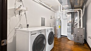 Une buanderie équipée d’un lave-linge et d’un sèche-linge à chargement frontal, d’un chauffe-eau et de tuyauteries apparentes.