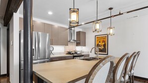Une cuisine moderne dotée d’un îlot central, d’appareils électroménagers en acier inoxydable et de luminaires suspendus.
