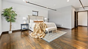Une chambre moderne avec un grand lit, des lampes de chevet, une plante en pot et un plaid en fausse fourrure.