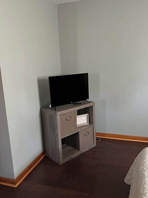 A corner room with a television on a wooden stand, a small shelf, and a white wall.