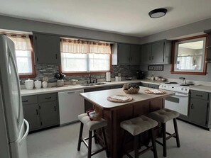 Uma cozinha moderna com armários cinza, uma ilha central com bancos, fogão e lava-louças.
