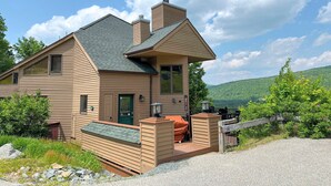 A two-story house with a sloped roof, a covered deck, and a view of a forested hillside.