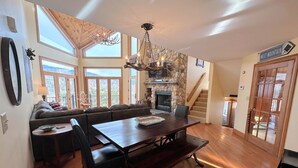 A spacious living area with a stone fireplace, wooden flooring, a large dining table, and a cozy seating area.