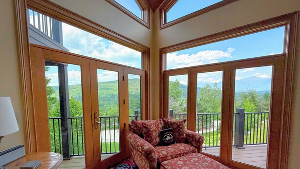 A spacious room with large sliding glass doors leading to a balcony, a floral sofa, and a small table with a lamp.