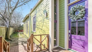 Ein schmaler Holzweg führt zu einem Haus mit einer violetten Tür und einem Kranz.