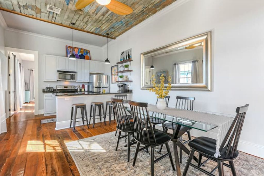 A spacious kitchen with white cabinets, a central island with stools, and a dining area with a glass table and black chairs.