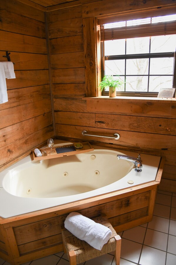 A wooden bathroom with a bathtub, a window with a plant, a towel rack, and a wooden chair. - The Blue Door Cabin: Charming, All-Wood w/Screened-in Porches - quiet & relaxing (Townsend)