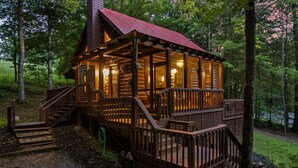A wooden cabin with a porch and stairs, surrounded by trees.