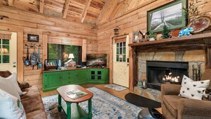 A cozy cabin interior with wooden walls, a green kitchen, a fireplace, and a comfortable seating area.