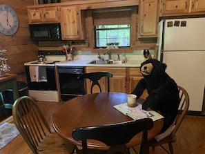 A wooden kitchen with a dining table, chairs, a refrigerator, a microwave, and a clock on the wall.