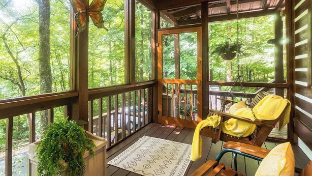 A wooden deck with a hanging chair, a hanging plant, and a view of the forest.