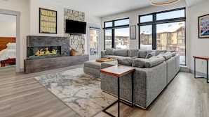A modern living room with a fireplace, large windows, and a sectional sofa.