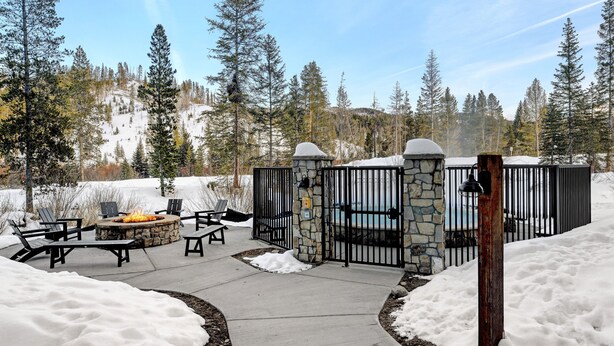 A stone fire pit with chairs, a pool, and a stone wall enclosure in a snowy outdoor area.