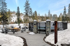 Un hogar de piedra con sillas, una piscina y un cerramiento de pared de piedra en un espacio exterior nevado.