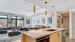 A modern kitchen with a large island, wooden cabinets, and pendant lights.