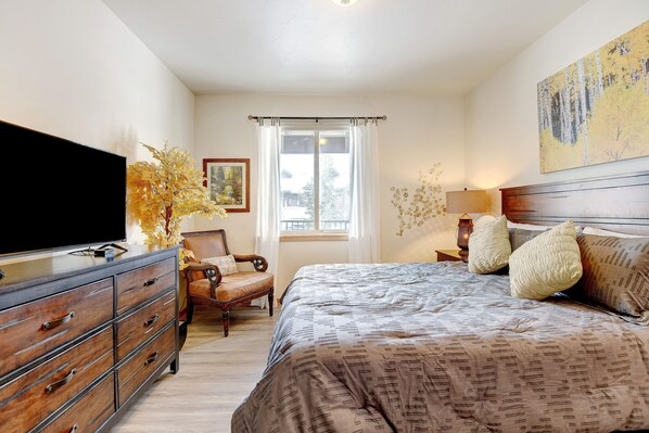 Un dormitorio con cama, cómoda, silla y un cuadro en la pared.