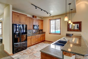 A kitchen with wooden cabinets, a black refrigerator, granite countertops, and pendant lighting.