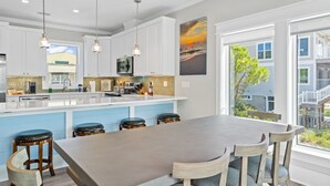 Cozinha moderna com armários brancos, uma ilha grande com banquetas, iluminação pendente e vista para o exterior.