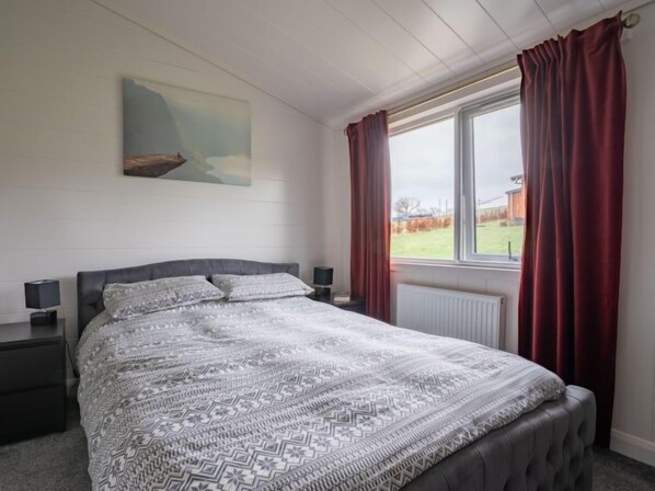 Un dormitorio con cama, dos mesitas de noche, una ventana con cortinas y un cuadro en la pared.